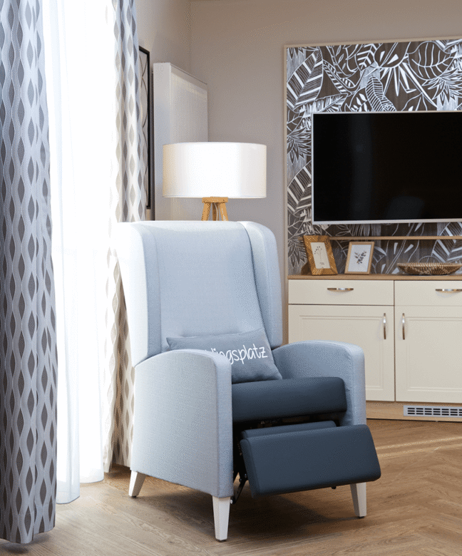 Ein modernes neu eingerichtetes Bewohnerzimmer einer Pflegeeinrichtung mit einem Pflegesessel in blau