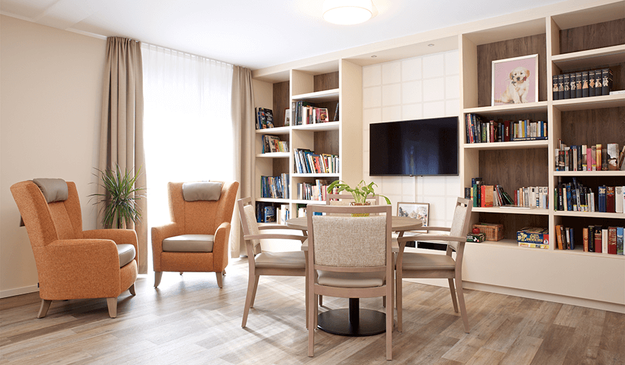 Gemeinschaftsraum Beispiel mit TV Regal und Büchern und gemütlicher Bestuhlung in Orange und Beige