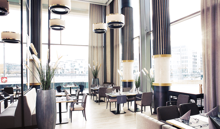 Einrichtungskonzept eines Restaurants mit hohen Wänden, natürlciher Beleuchtung und moderner Einrichtung.