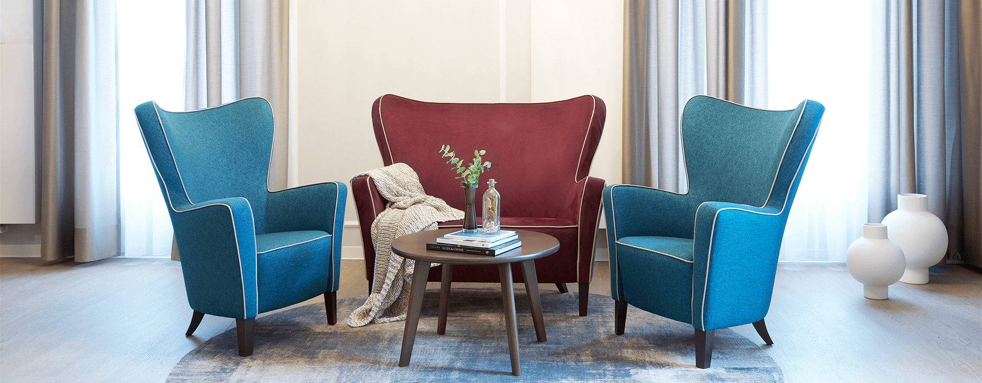 Gemeinschaftraum mit einer Sitzgruppe mit zwei blauen Sesseln und einem roten Sofa in der Mitte